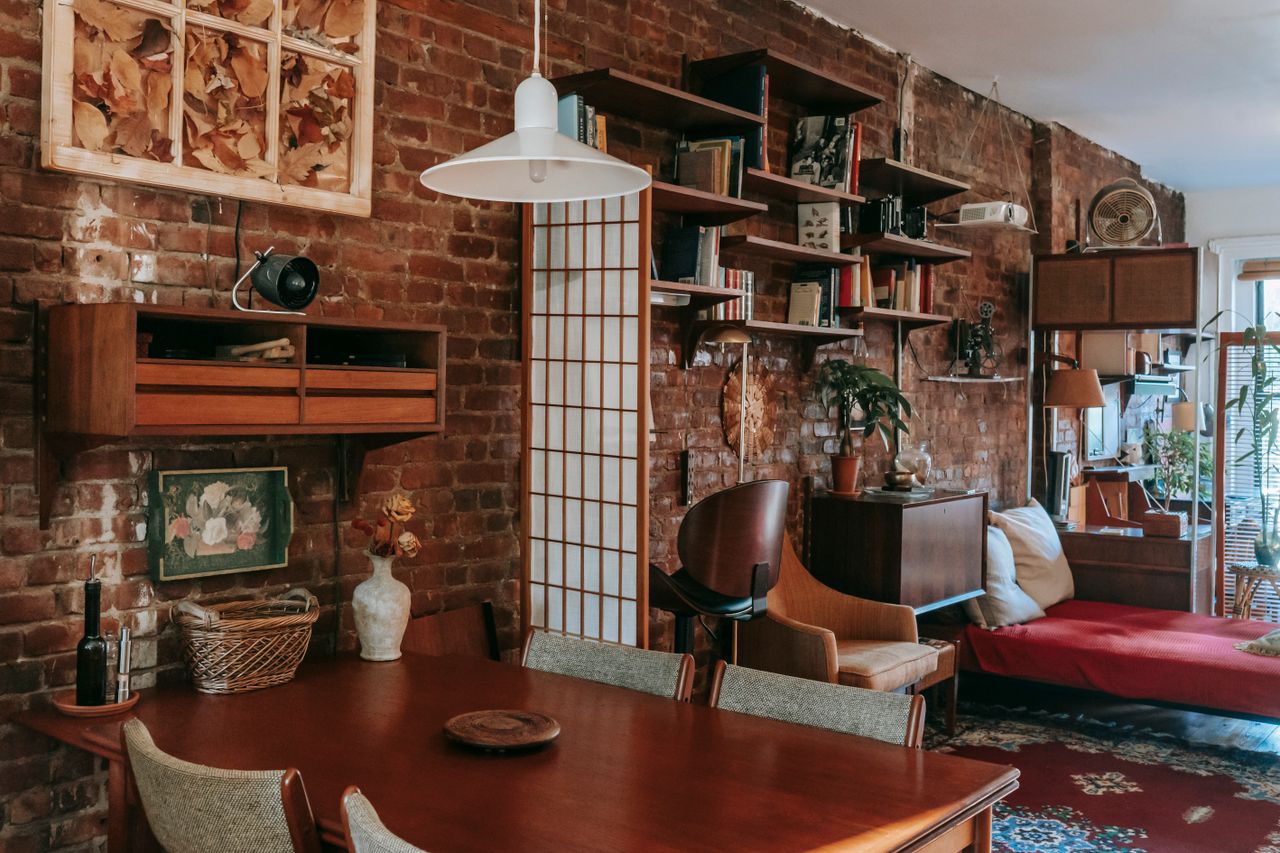 Mastering the First Impression: Your intriguing post title goes here Interior of cozy vintage styled dining room with classic wooden table and chairs placed near weathered brick wall decorated with paintings and bookshelves